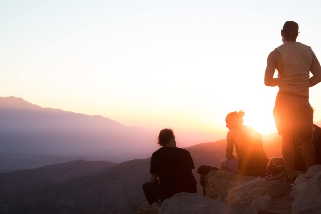 Silhouettes along mountain range with sun flare